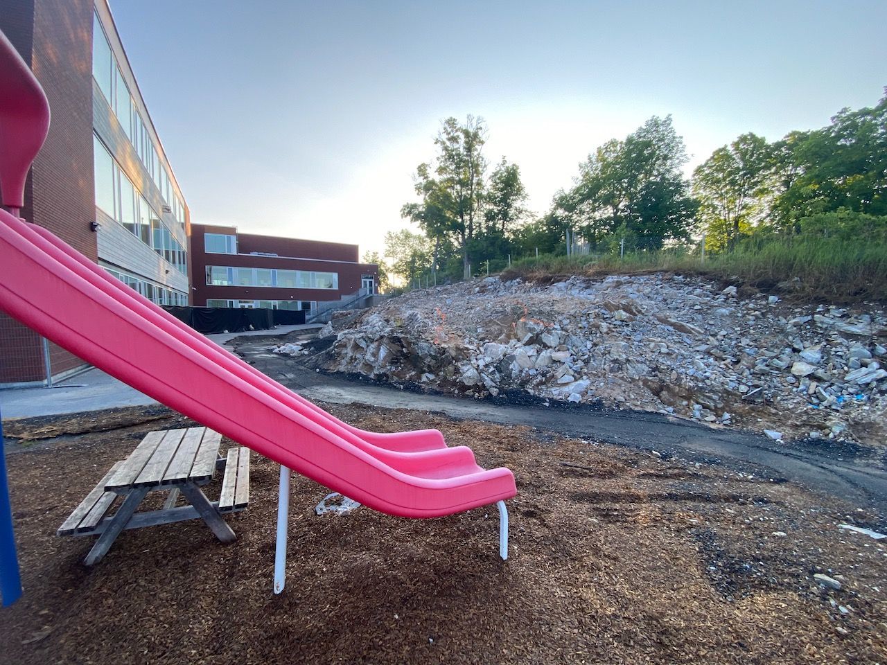 A pink slide is sitting next to a wooden picnic table in a playground.