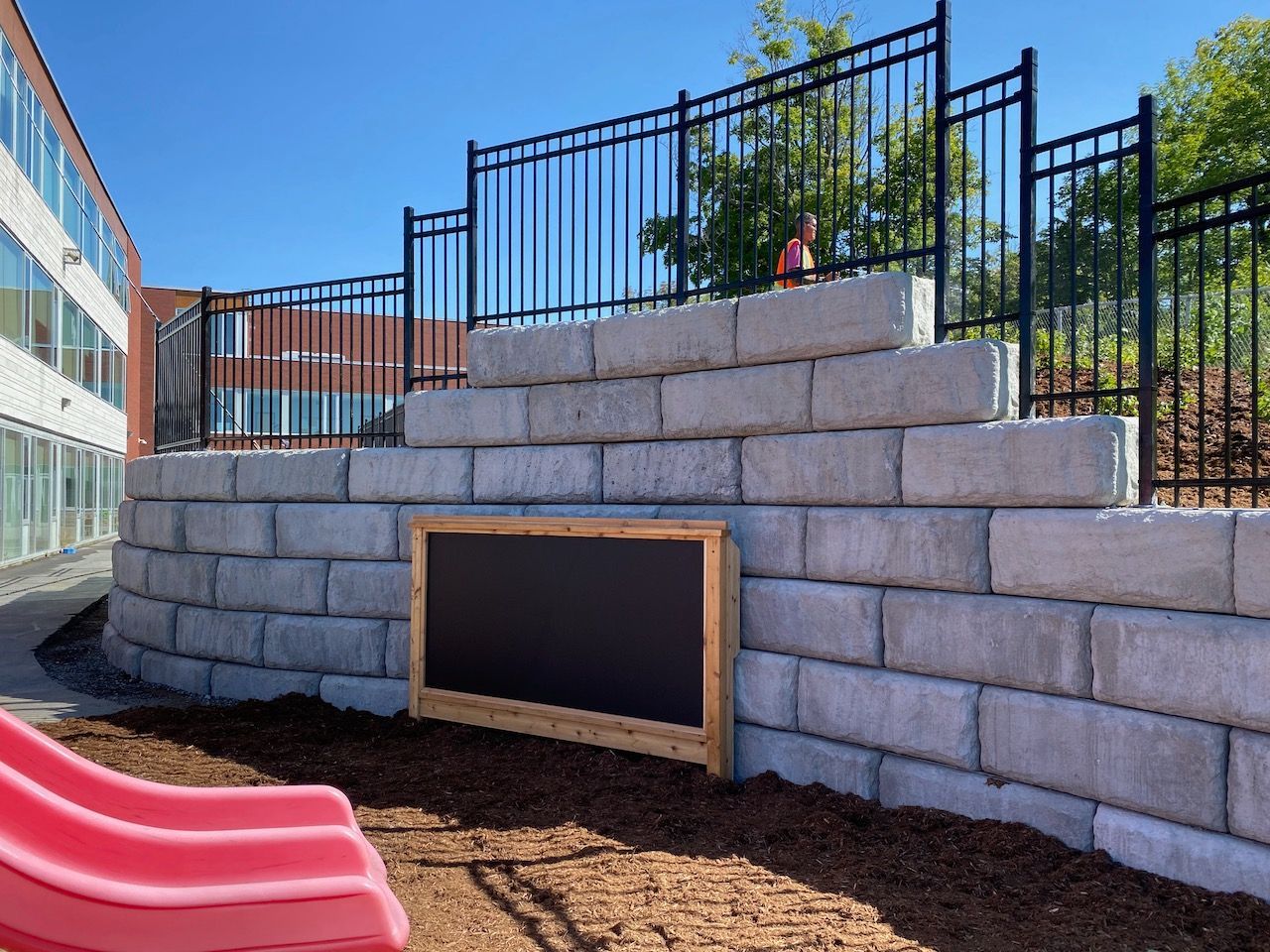 A child is sitting on a brick wall next to a slide.