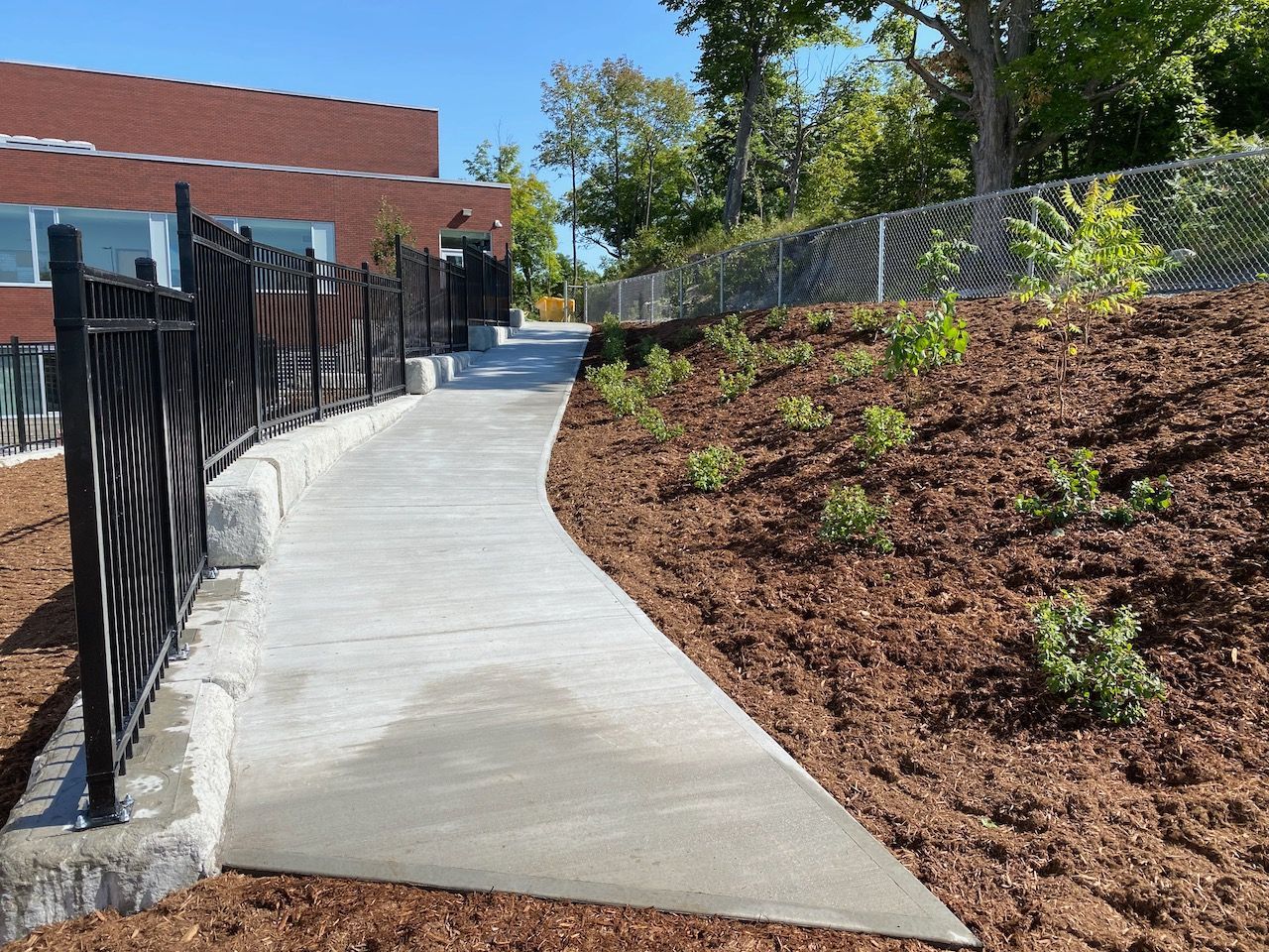 A concrete walkway leading to a building with a fence and mulch.