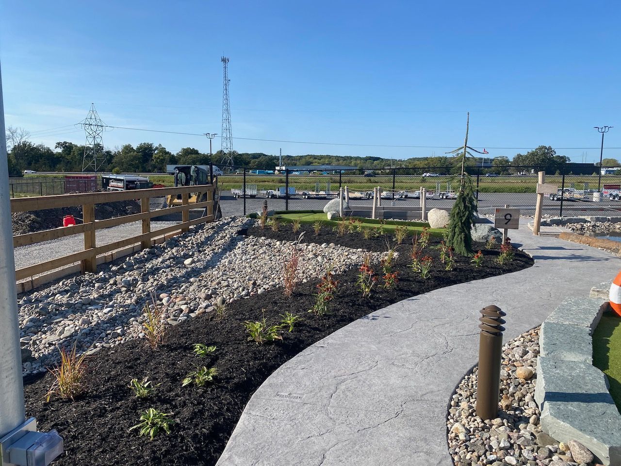 A concrete walkway surrounded by rocks and plants with a wooden fence in the background.