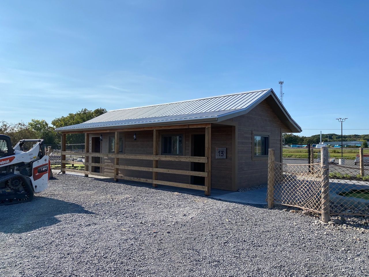 A small house with a porch is sitting in a gravel lot next to a bobcat.