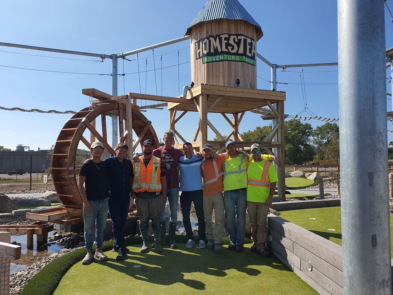 A group of men standing in front of a water tower that says homestead