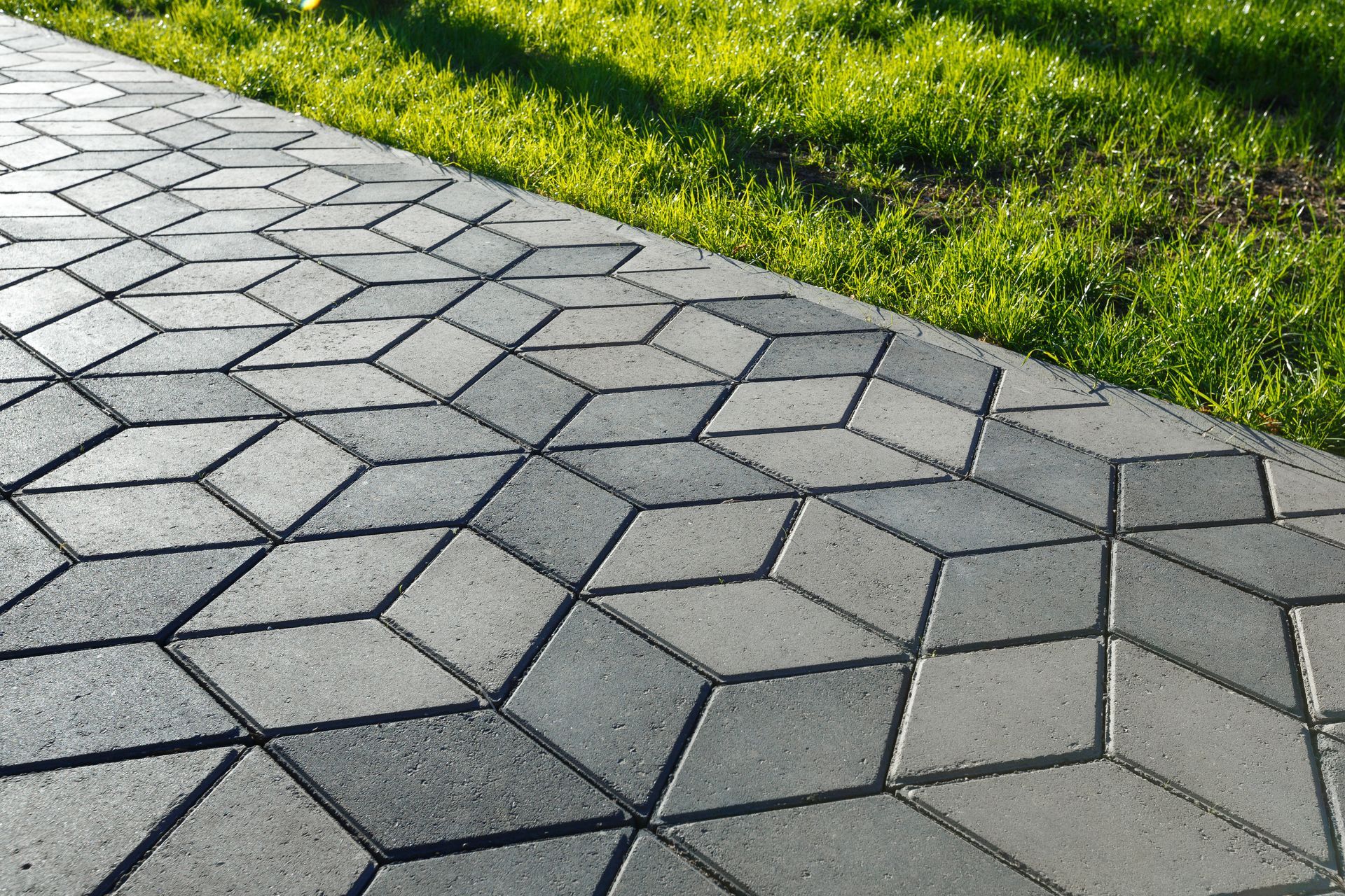 A brick walkway with a geometric pattern and grass on the side.