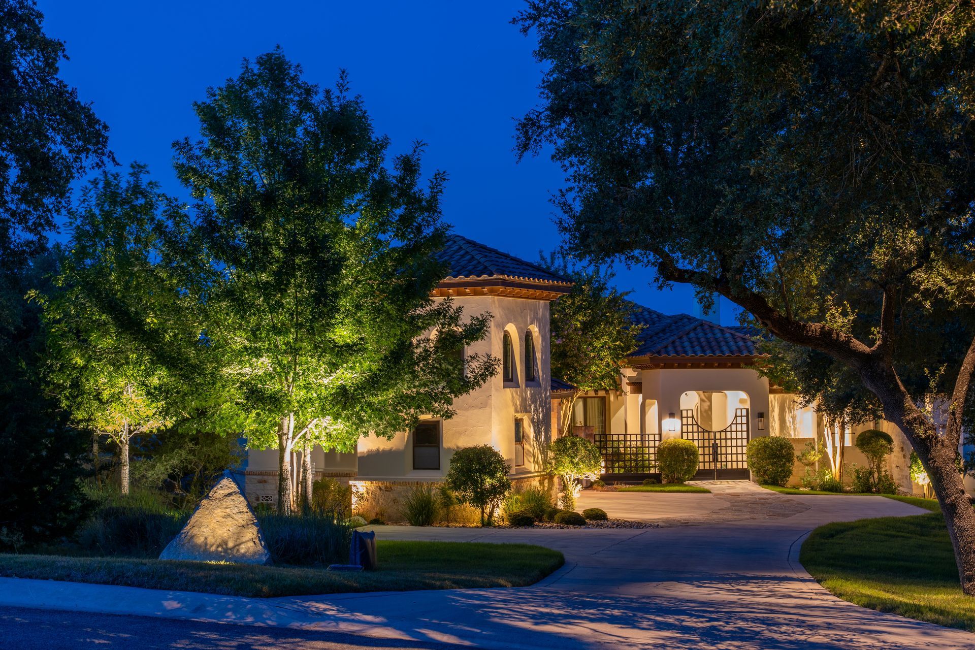 A large house is lit up at night with trees in front of it.