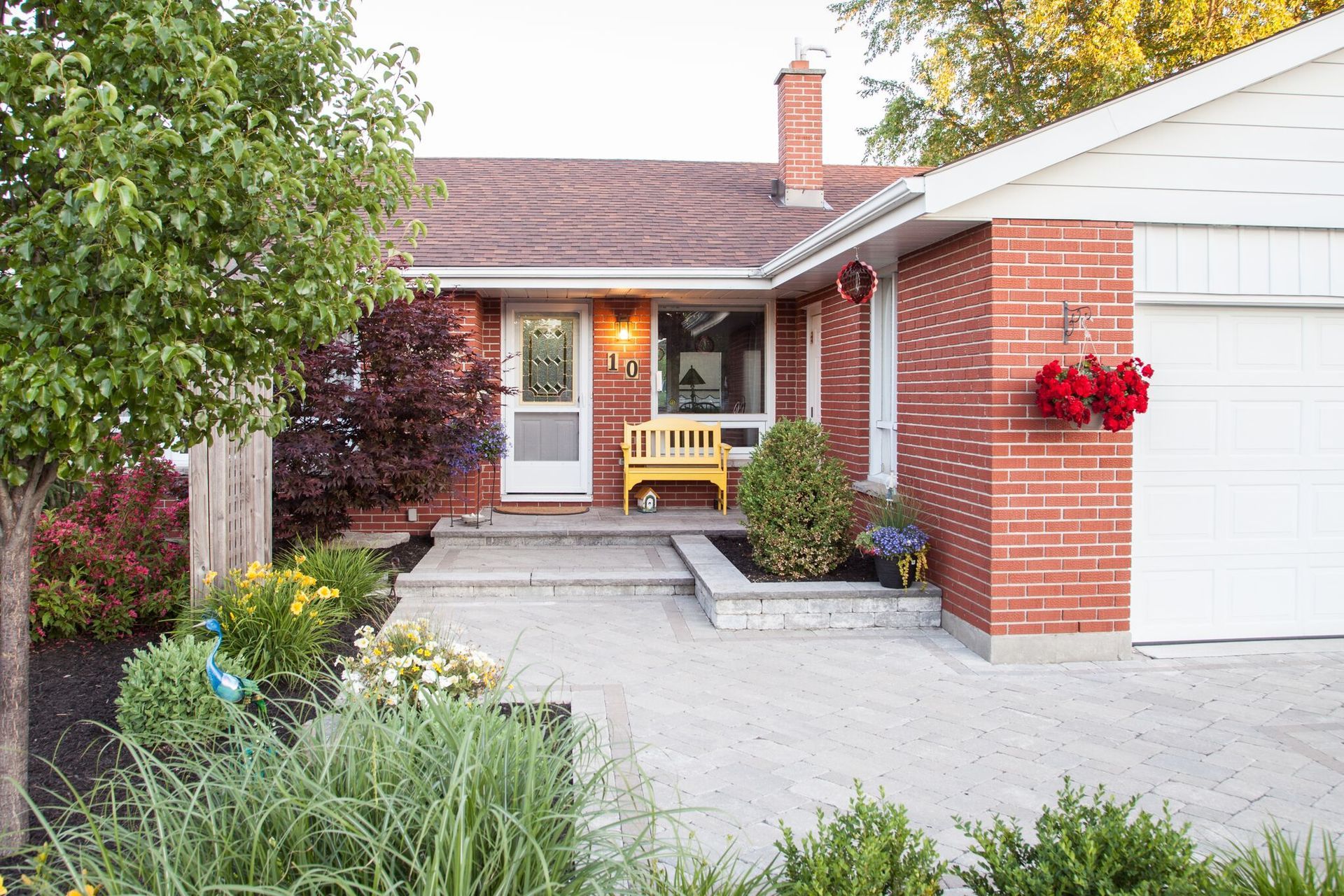 A brick house with a white garage door and a yellow bench in front of it.