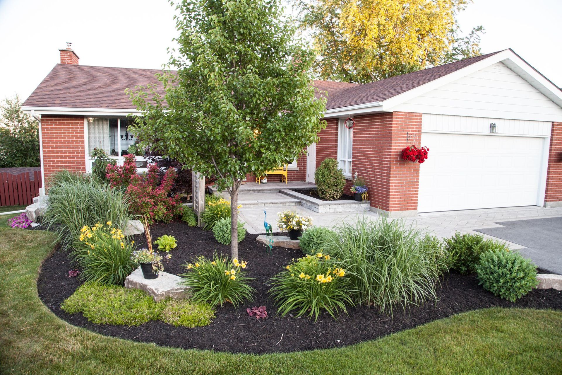 A brick house with a white garage door and a garden in front of it.