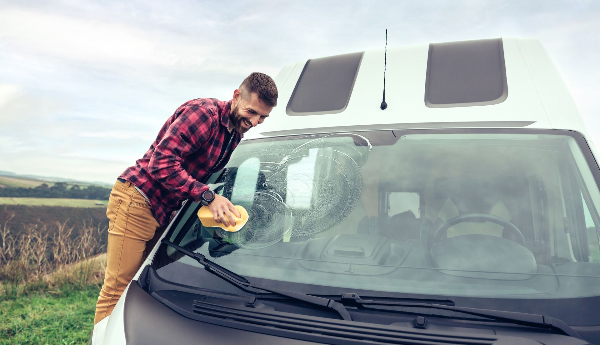 Man cleaning camper van glass with sponge outdoor.