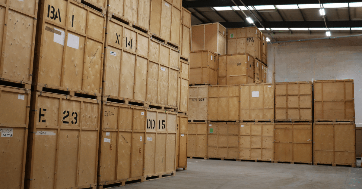A person and a partner sit on a wood floor, packing belongings into cardboard boxes amidst moving supplies.