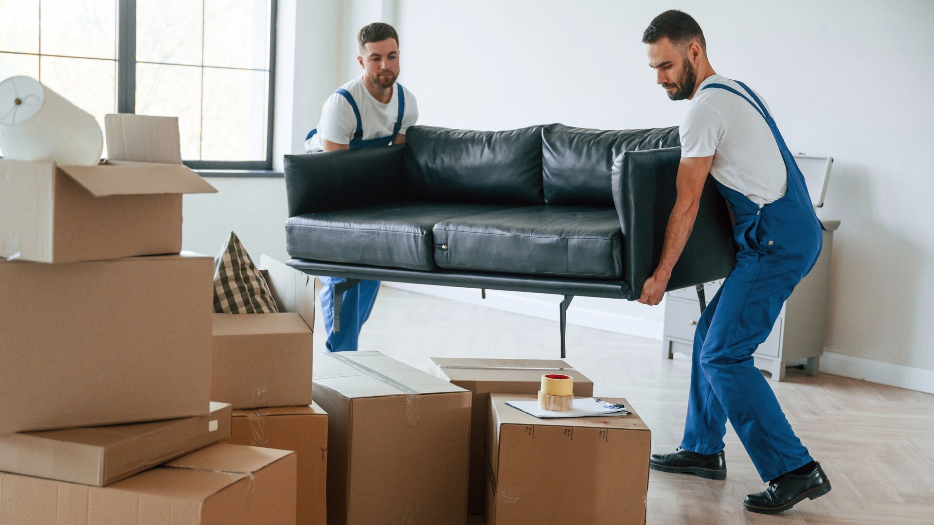 Four people move a large appliance up a ramp and into a parked red moving truck in a parking lot.