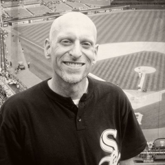 a man wearing a white sox shirt smiles in front of a baseball field
