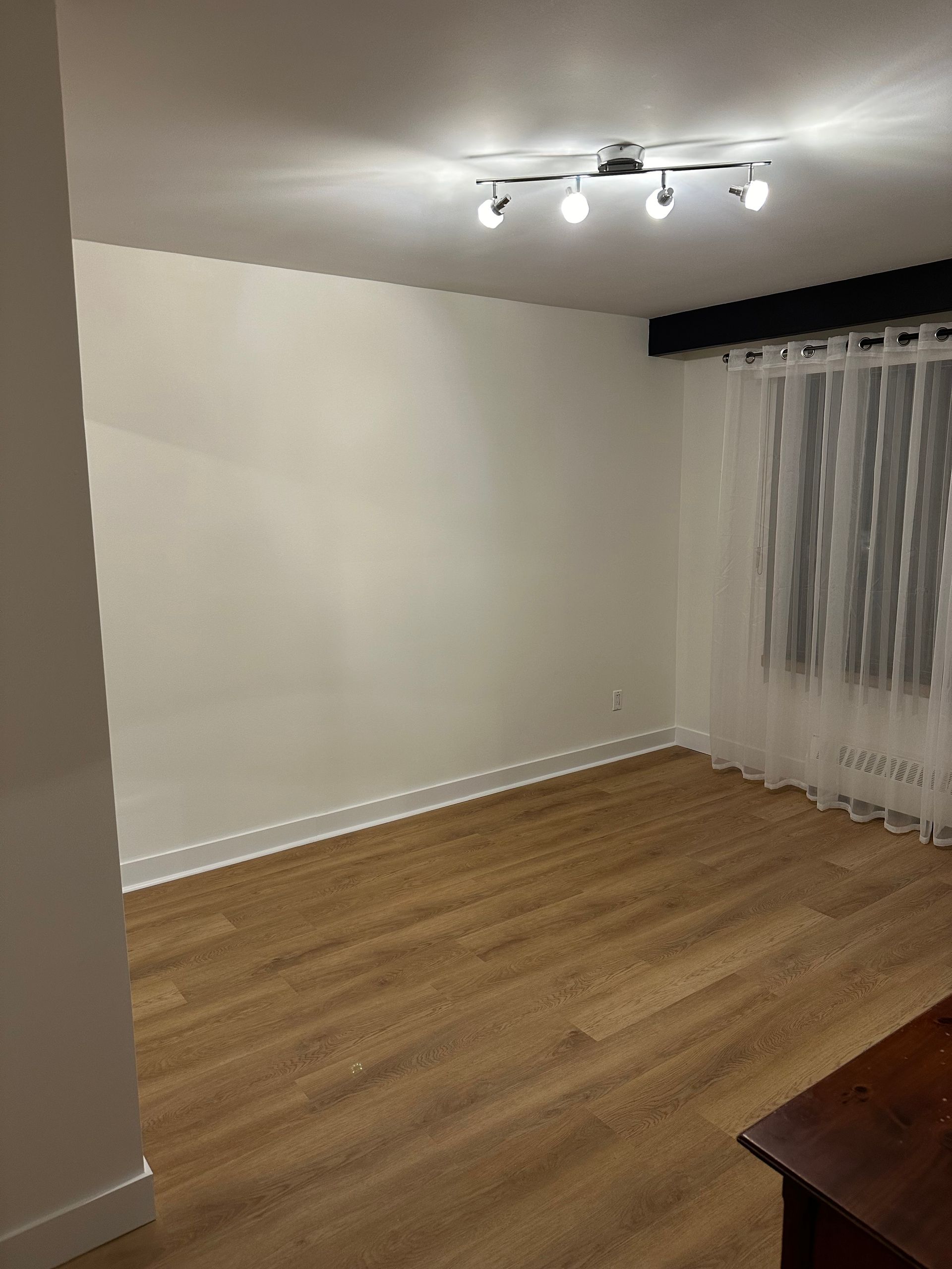 Un salon vide avec du parquet et des murs blancs.