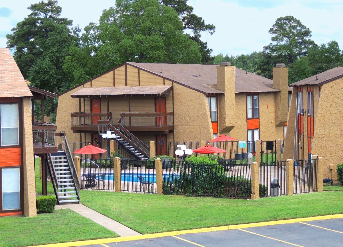 An exterior view of Kingwood Forest Apartments with a large tree and view of pool