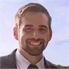 A man with a beard is wearing a suit and tie and smiling.