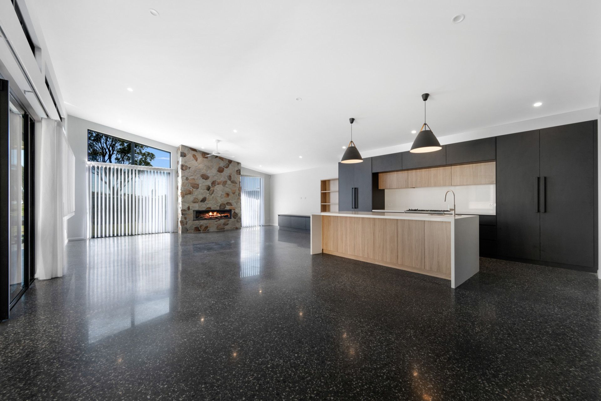 Open-plan kitchen and living area with black speckled floor, wooden island, and stone fireplace — L & K Electrical & Air Conditioning in Tamworth, NSW