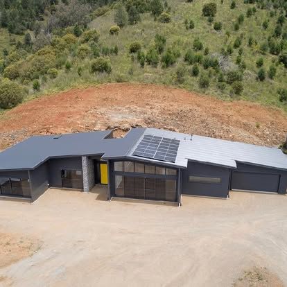 Modern grey house with solar panels on the roof; yellow front door, in a hillside setting — L & K Electrical & Air Conditioning in Barraba, NSW