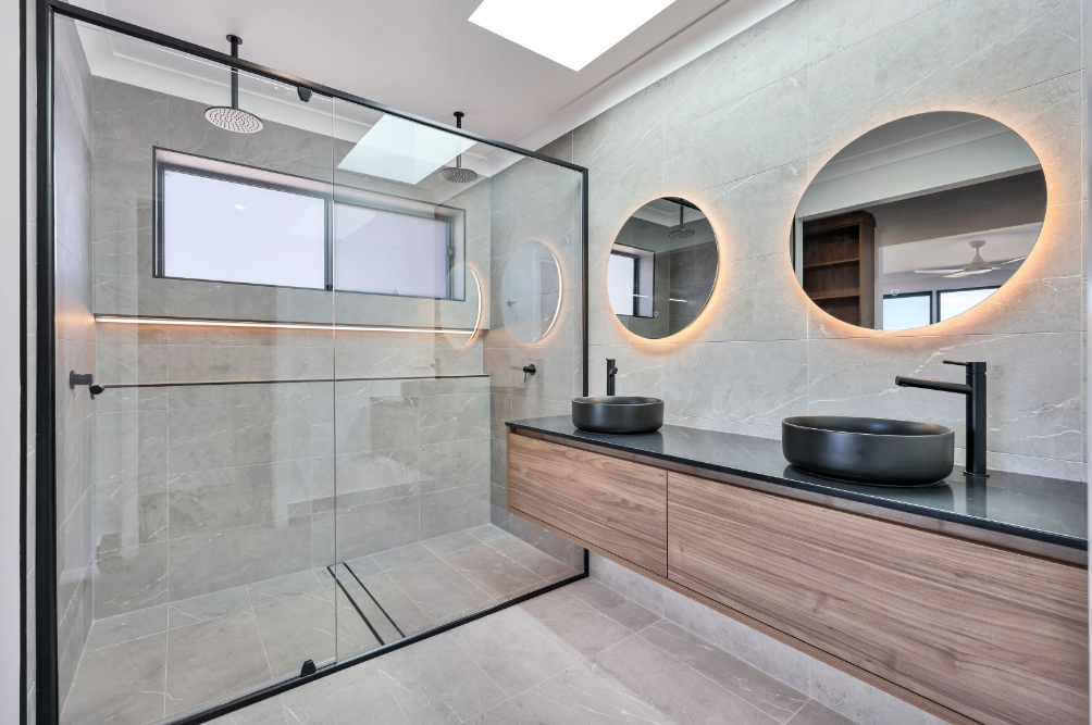 Modern bathroom with a glass shower, two round lighted mirrors, and a wood vanity — L & K Electrical & Air Conditioning in Barraba, NSW