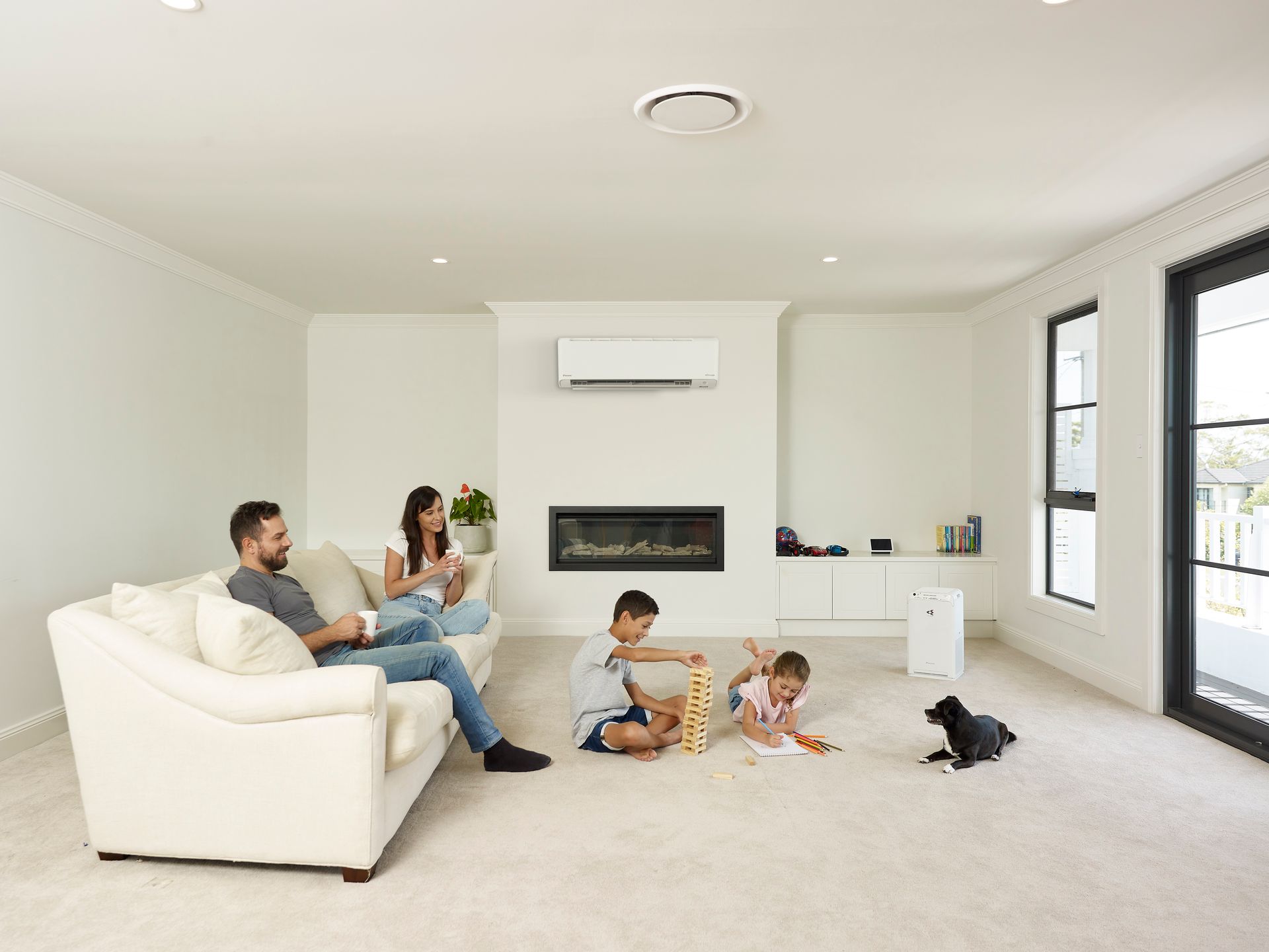 Family relaxing in a modern living room with fireplace and white walls; two children play — L & K Electrical & Air Conditioning in Scone, NSW