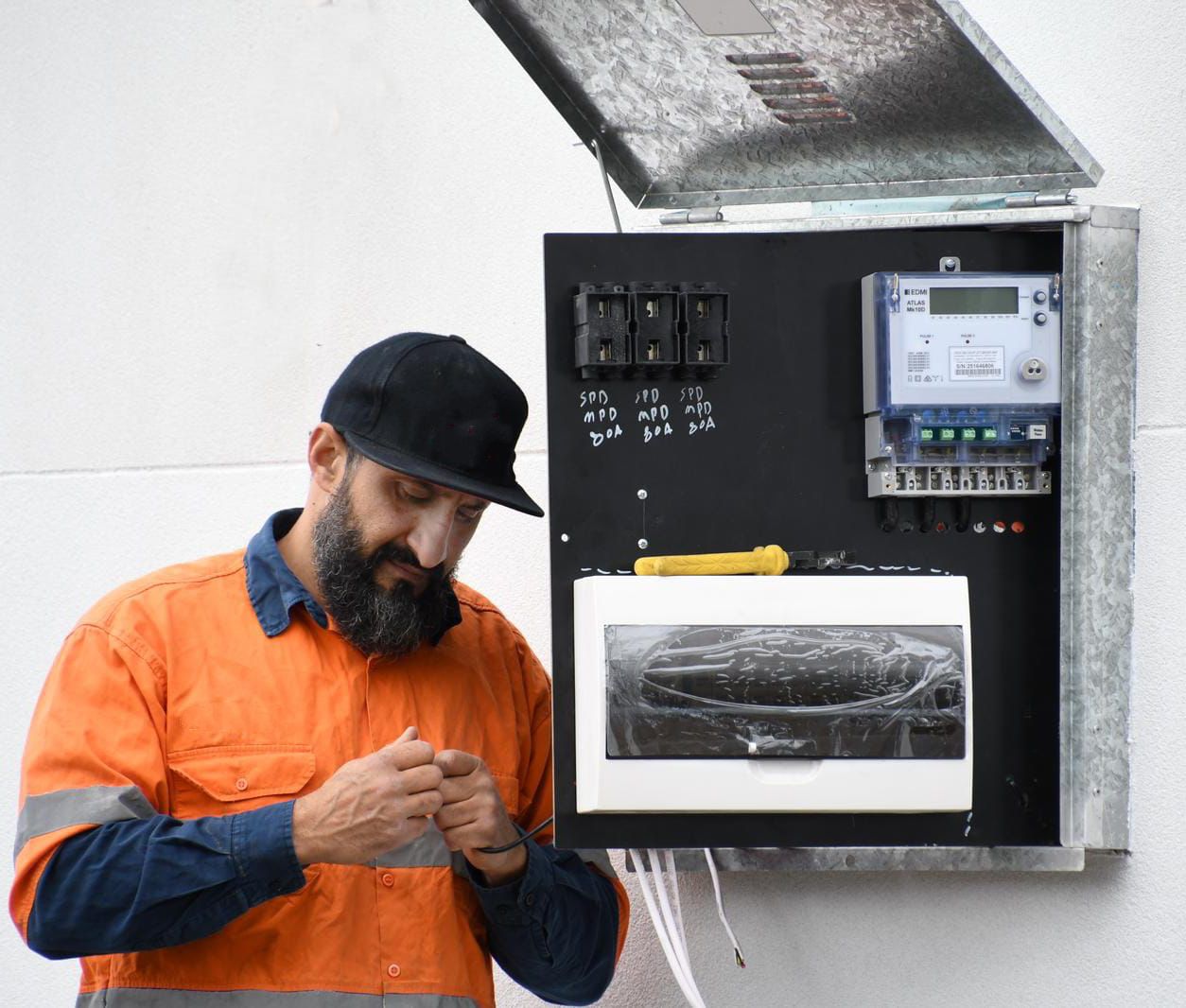 Electrician in work clothes looking at an open electrical panel on a wall, inspecting wiring — L & K Electrical & Air Conditioning in Scone, NSW