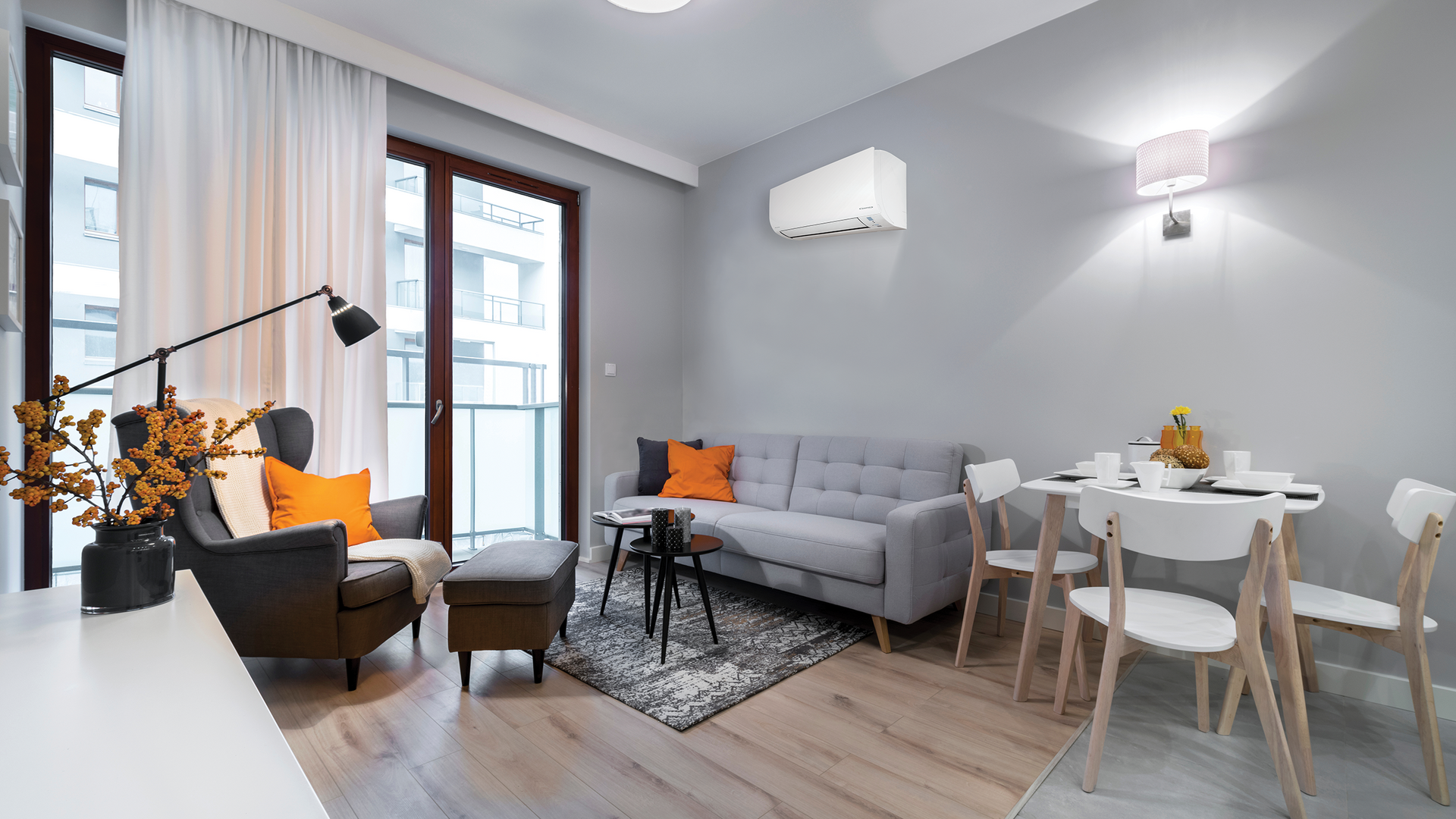 Modern living room with grey sofa, arm chair, small table, and dining area; balcony doors — L & K Electrical & Air Conditioning in Tamworth, NSW