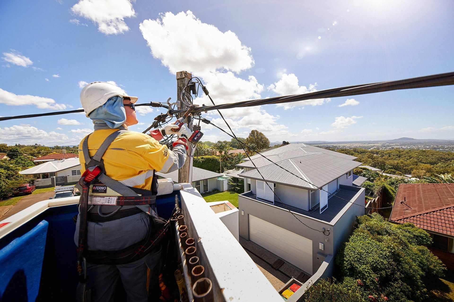 Line worker in a bucket truck repairs overhead power lines on a sunny day over residential homes — L & K Electrical & Air Conditioning in Tamworth, NSW