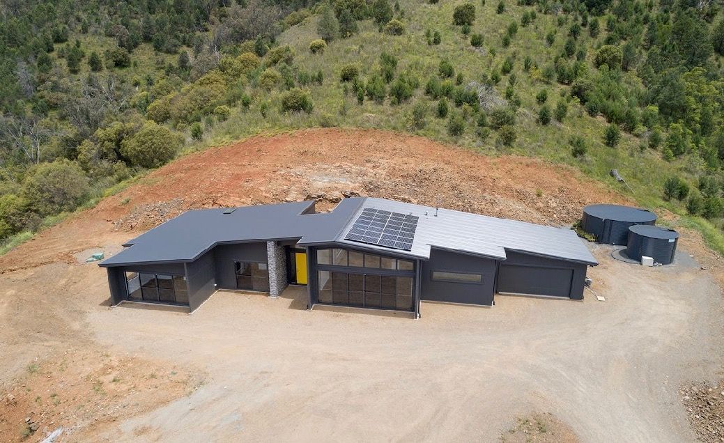 Modern grey house with solar panels on a hillside, with water tanks nearby — L & K Electrical & Air Conditioning in Tamworth, NSW