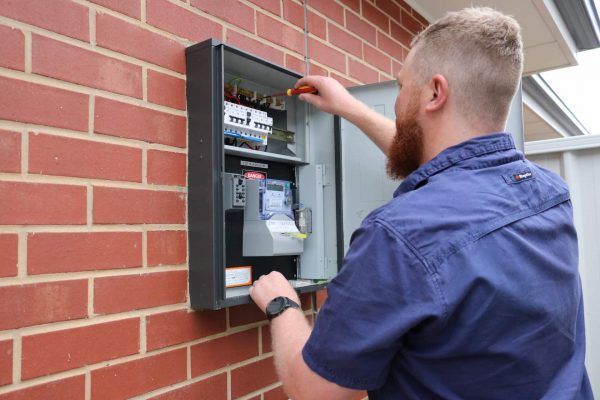 Electrician working on an electrical panel mounted on a red brick wall — L & K Electrical & Air Conditioning in Uralla, NSW