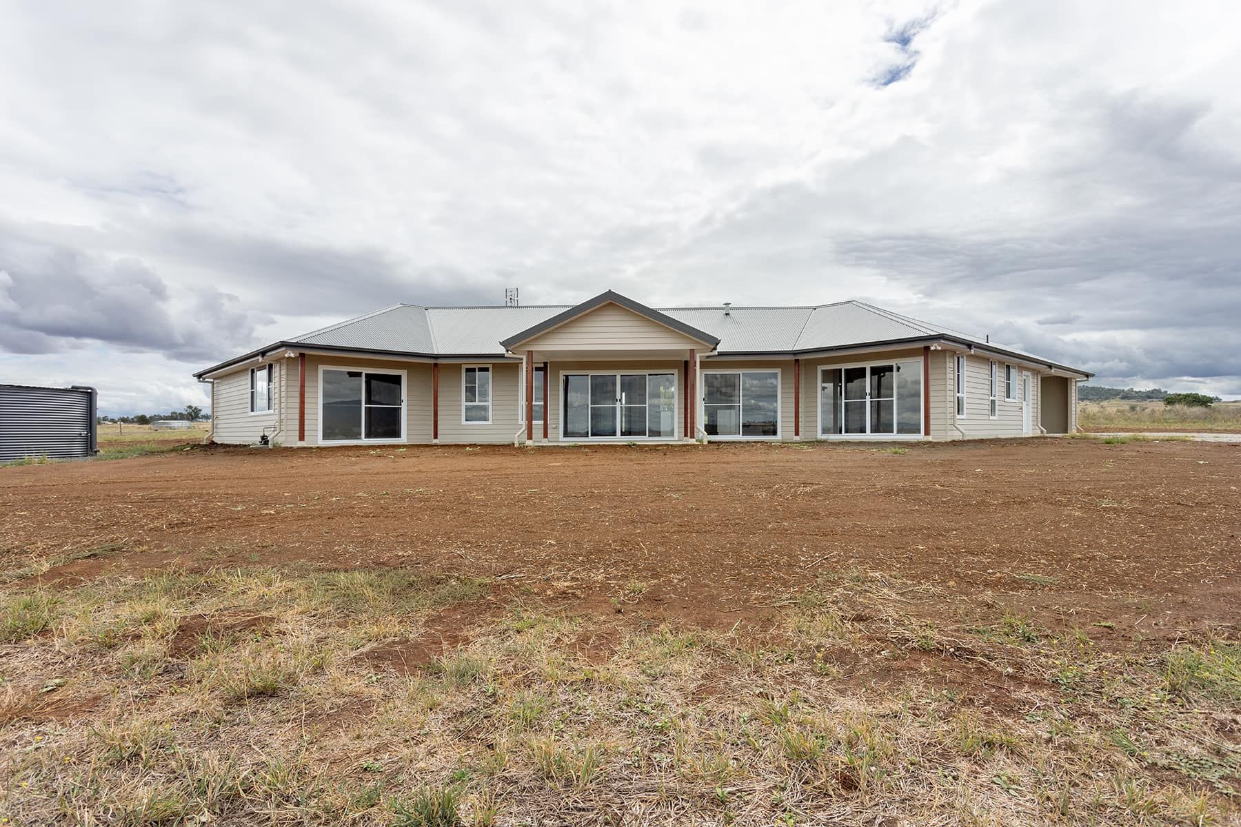 Single-story house with large windows on a brown, grassy plain under a cloudy sky — L & K Electrical & Air Conditioning in Uralla, NSW