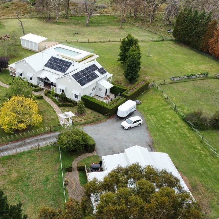 Aerial view of a white house with solar panels, a pool, and a car on a grassy property.