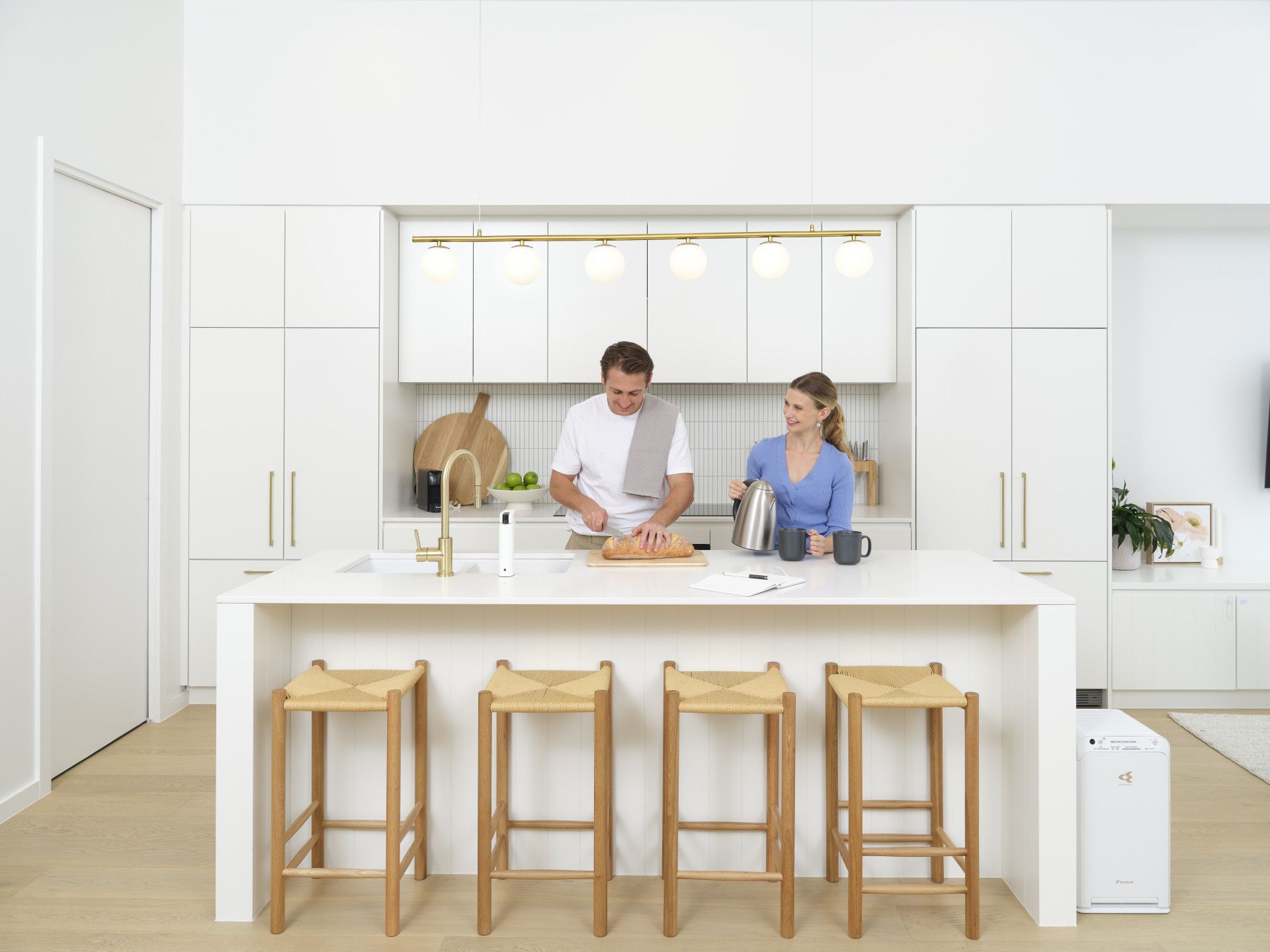 A man and woman prepare food at a kitchen island with stools. White cabinets, gold accents, light wood floors — L & K Electrical & Air Conditioning in Tamworth, NSW