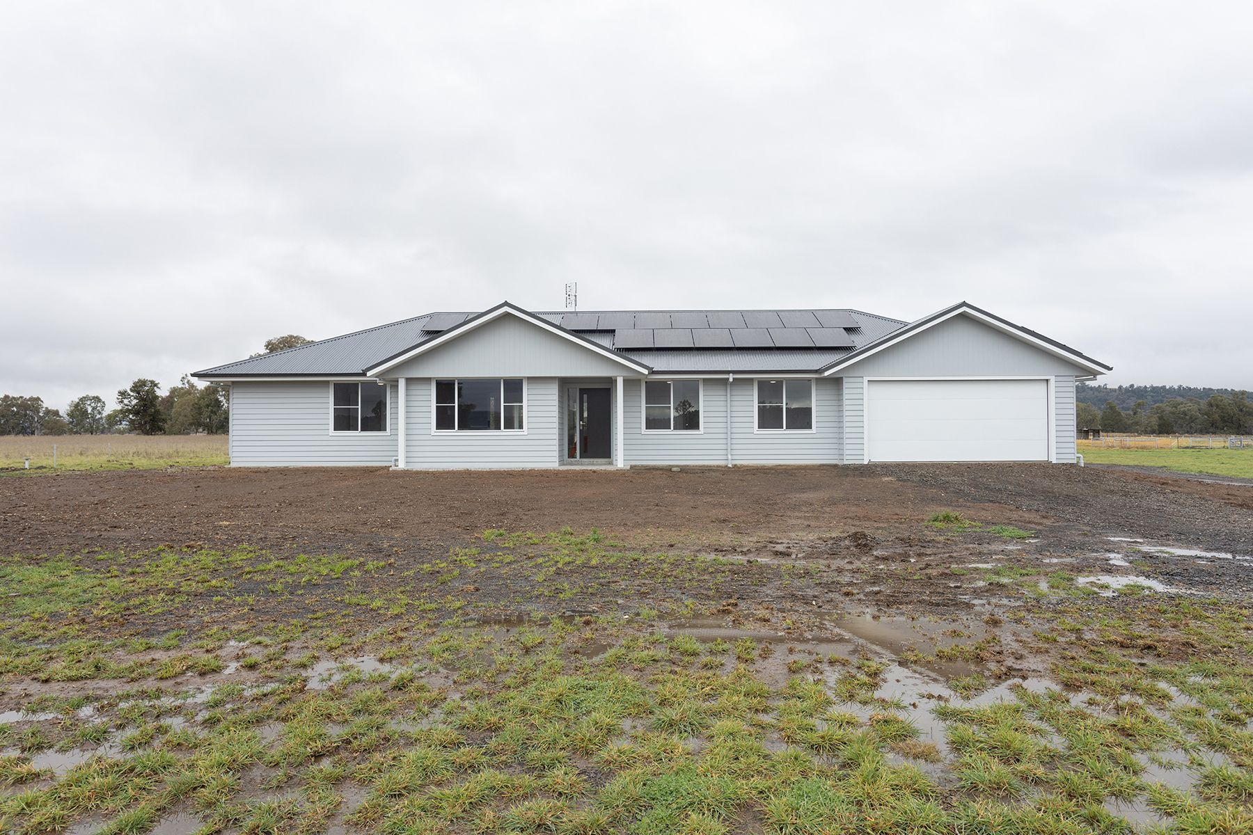 Grey ranch-style house with attached garage on a muddy, grassy lot under a cloudy sky — L & K Electrical & Air Conditioning in Armidale, NSW