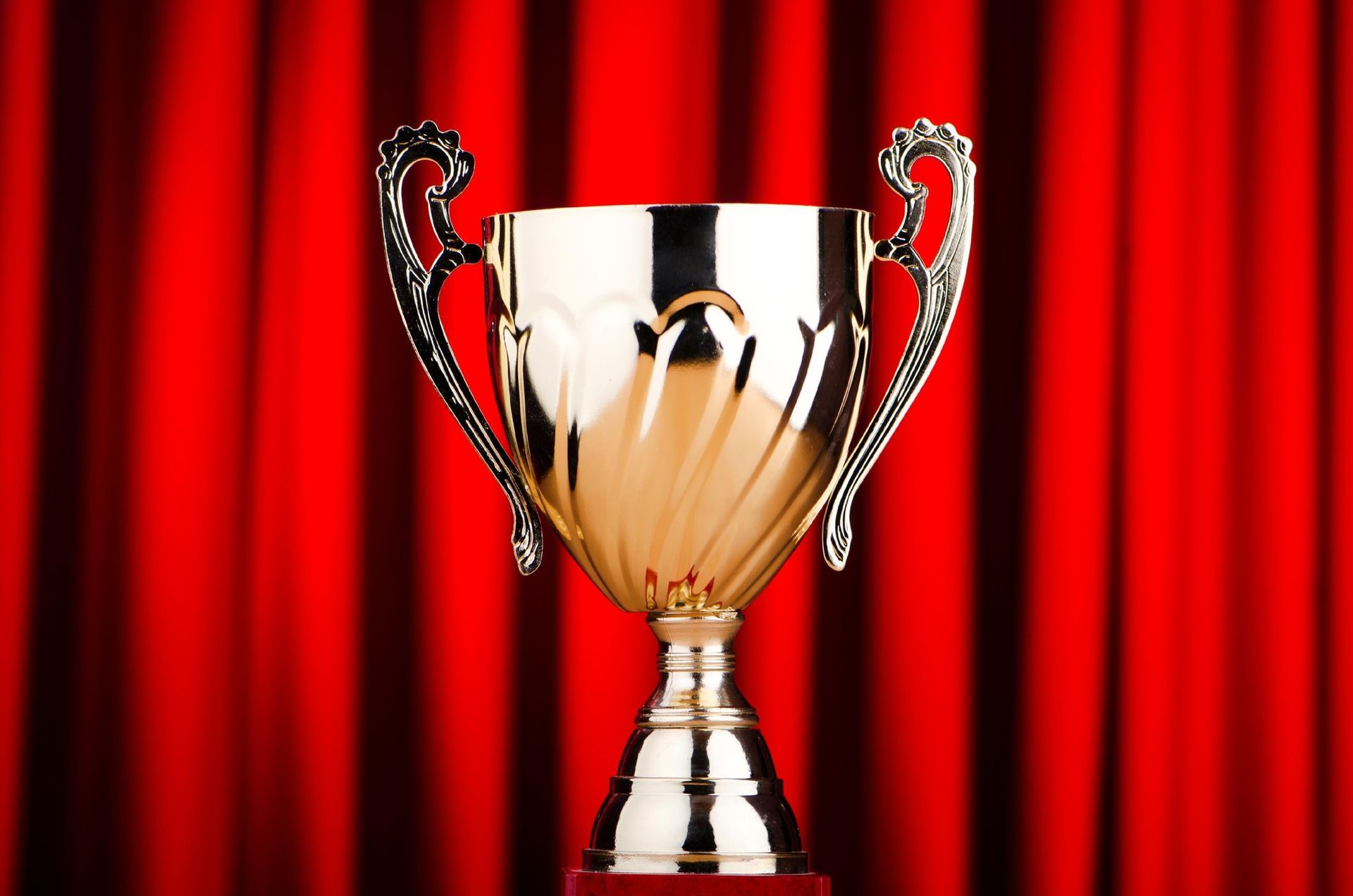 A silver trophy is sitting in front of a red curtain.