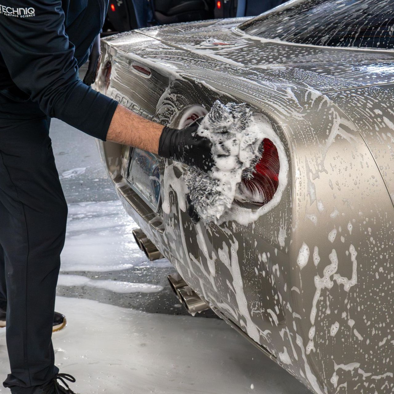 A man is washing a black car with soap and water.