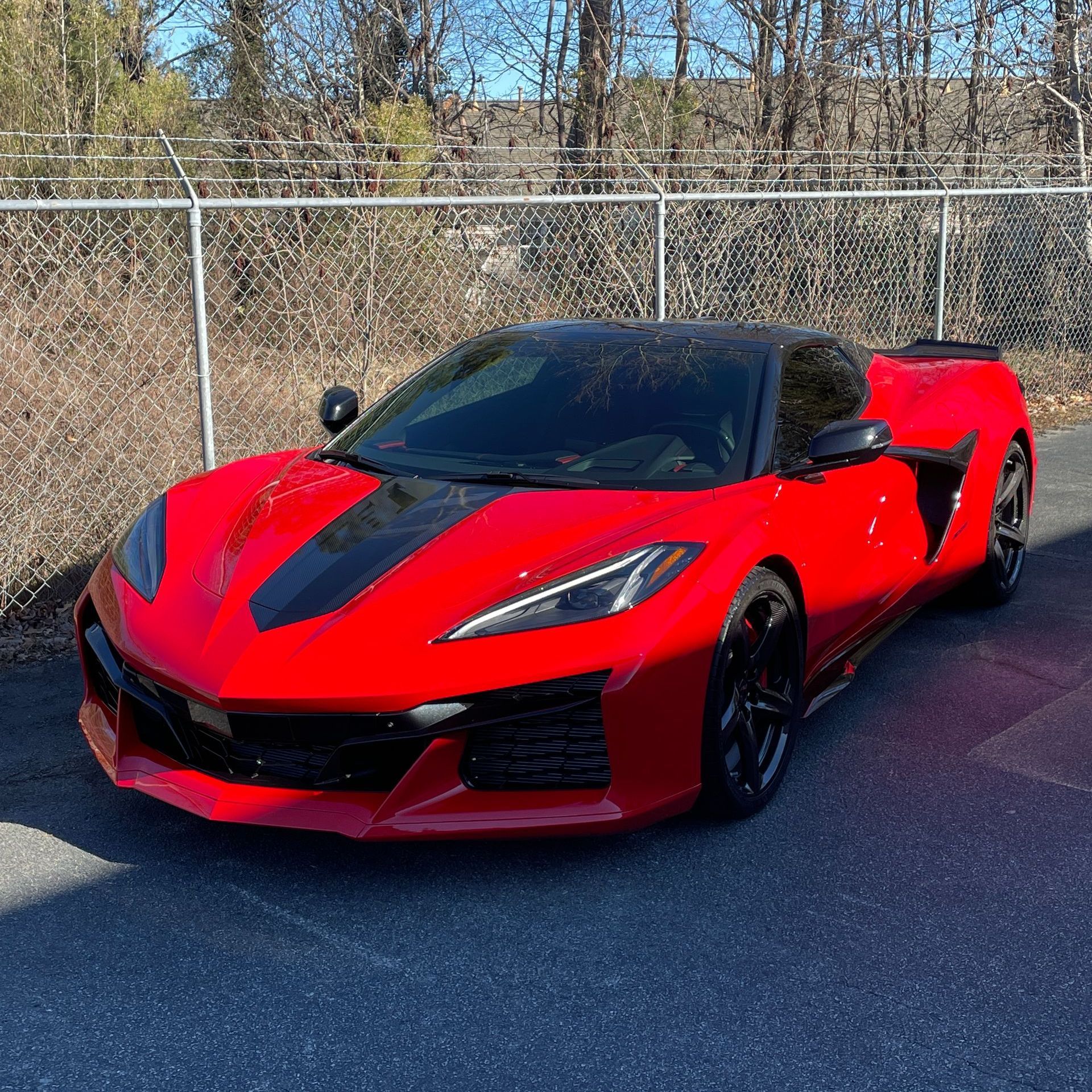 A red corvette is parked on the side of the road next to a fence.