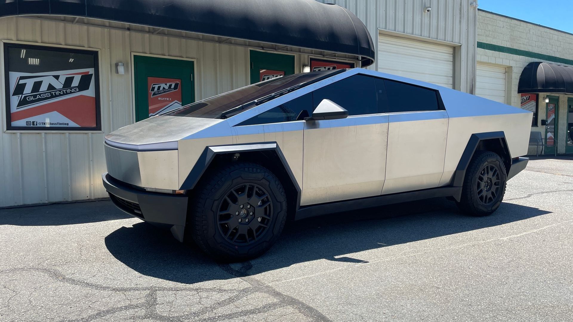 A silver tesla cybertruck is parked in front of a building.