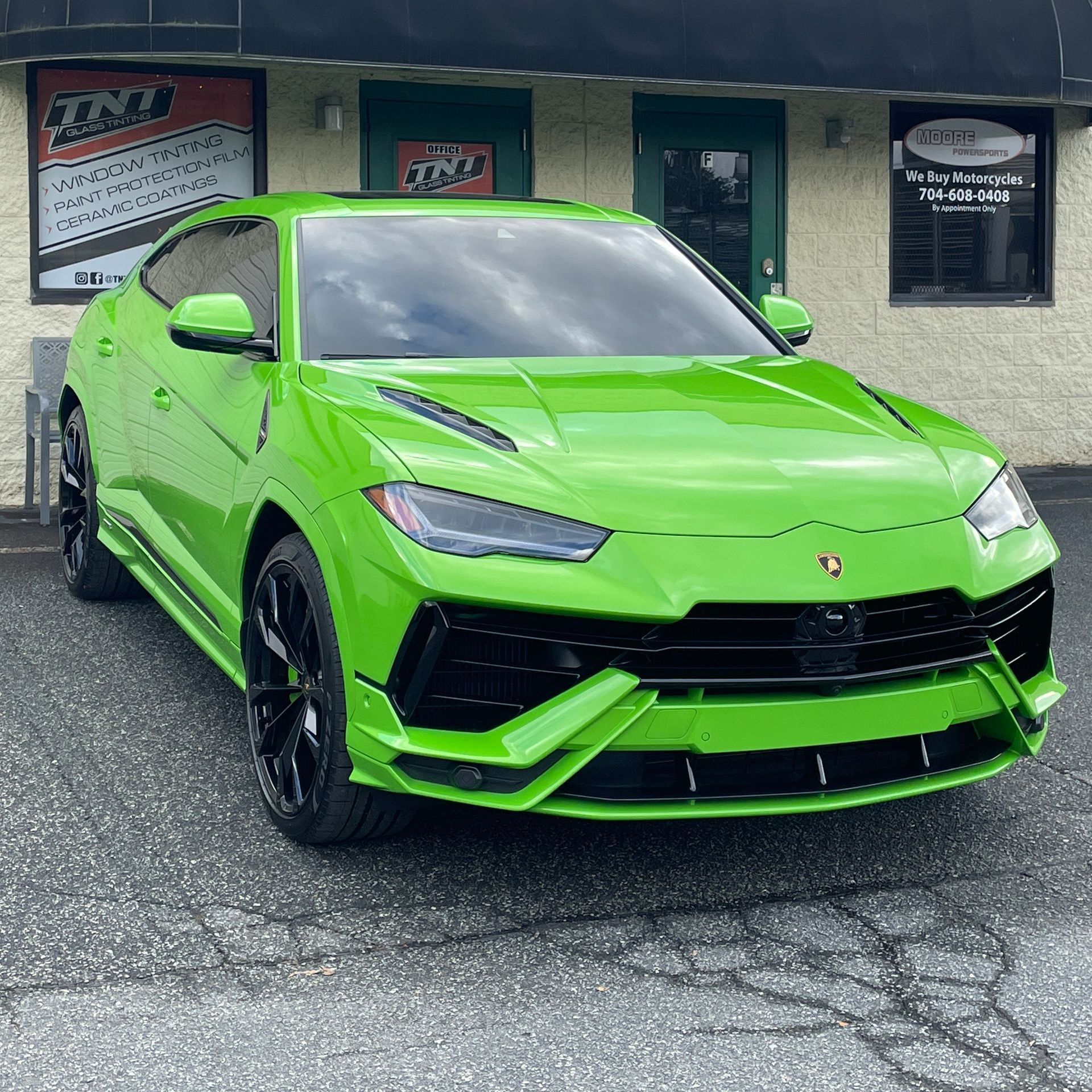 A green lamborghini urus is parked in front of a building.
