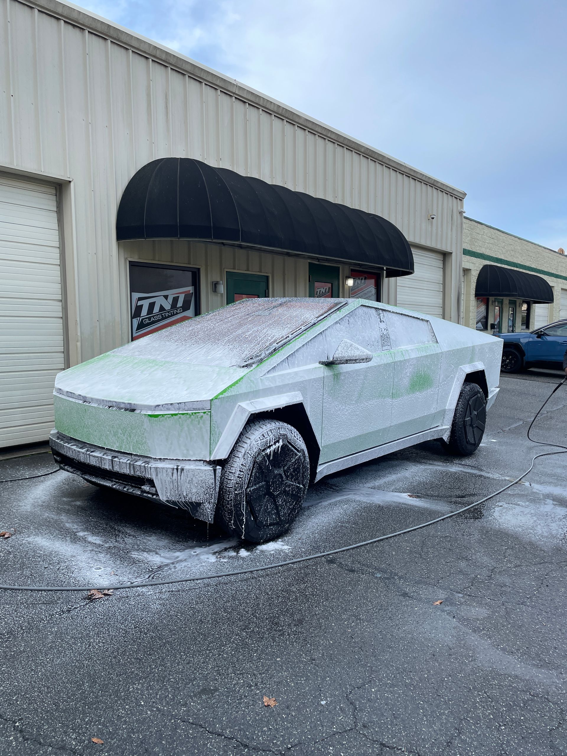 A tesla cybertruck is covered in foam in front of a building.