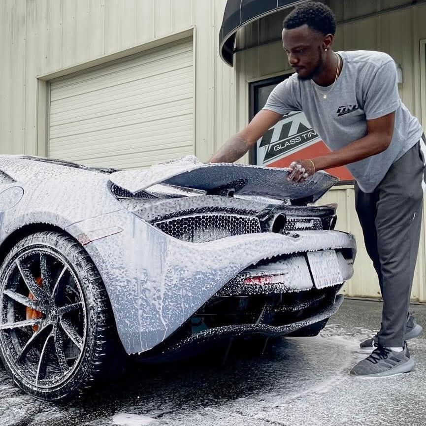 A man in a grey shirt is washing a car