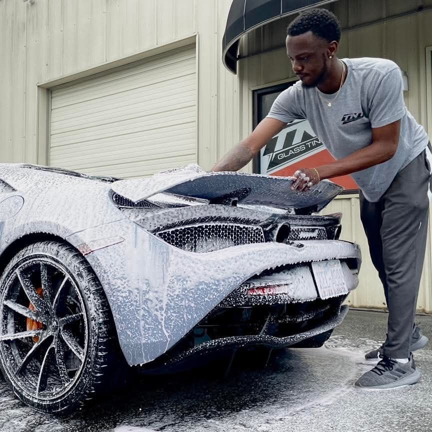A man in a grey shirt is washing a car