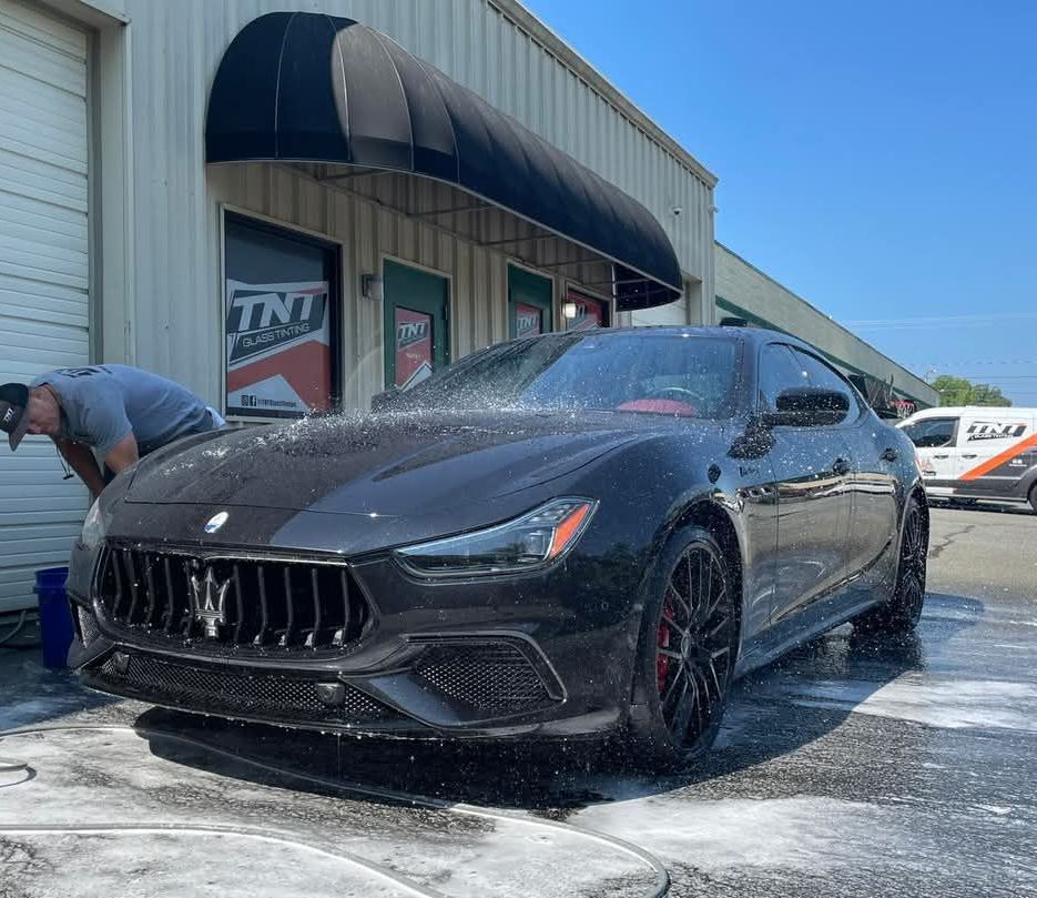 A man is washing a maserati outside of a garage.