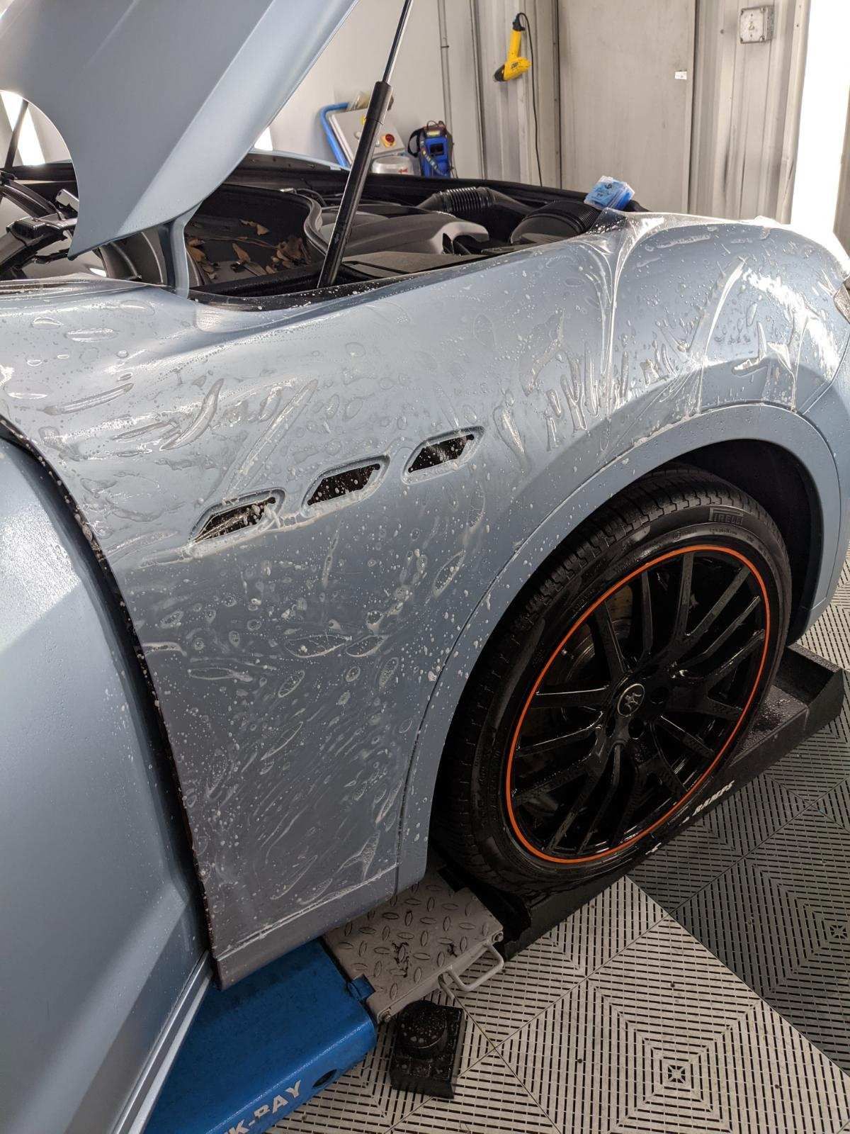 A car with the hood open is sitting on a lift in a garage.