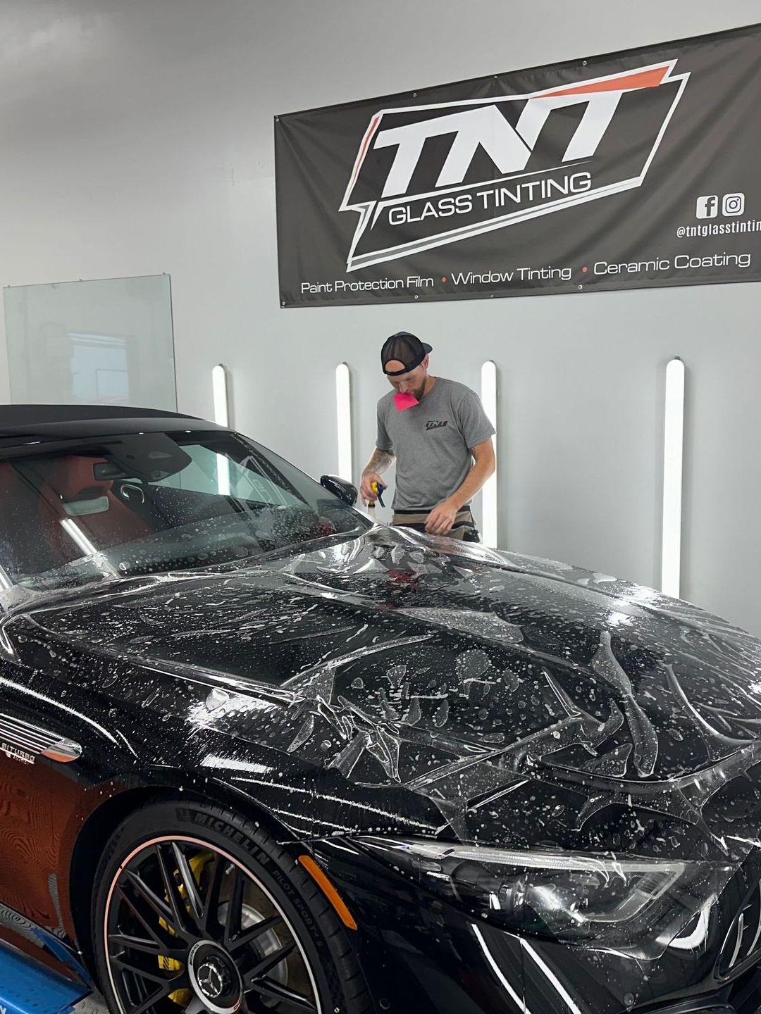 A man is covering a black car with a clear film.
