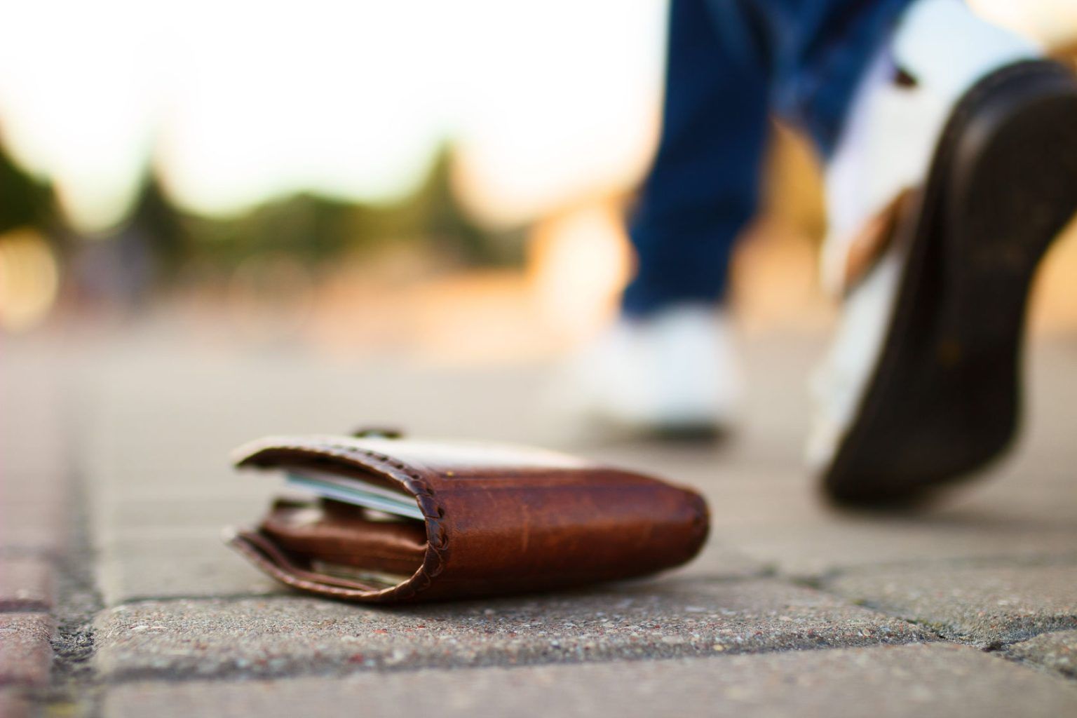 A person is walking past a wallet on the sidewalk.