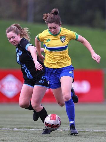 Two women are playing soccer on a field and one of them is wearing a yellow shirt.