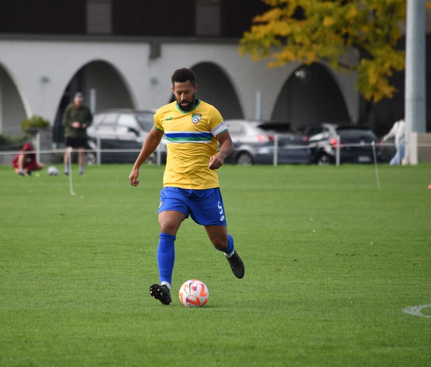 A man in a yellow shirt and blue shorts is kicking a soccer ball on a field.