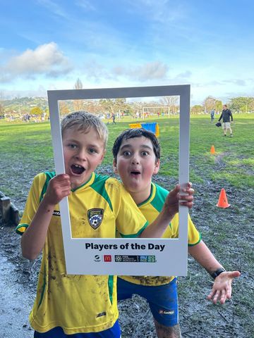 Two young boys are posing for a picture with a frame that says players of the day.