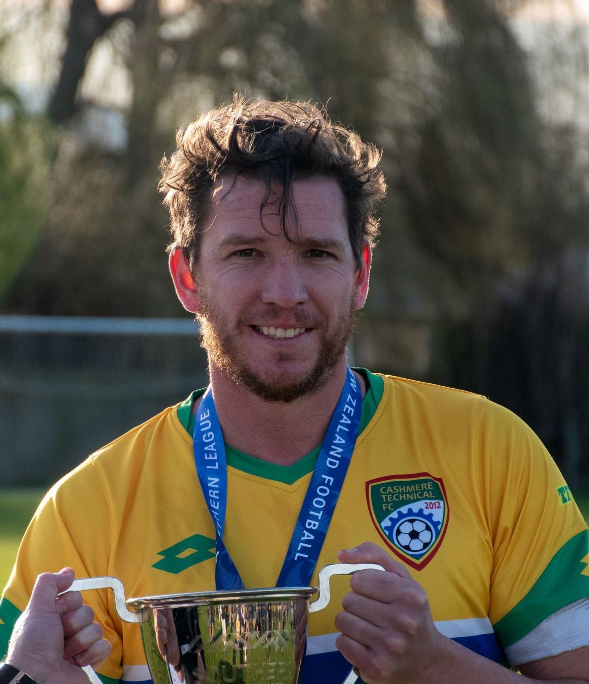 A young man is smiling and wearing a brown shirt.