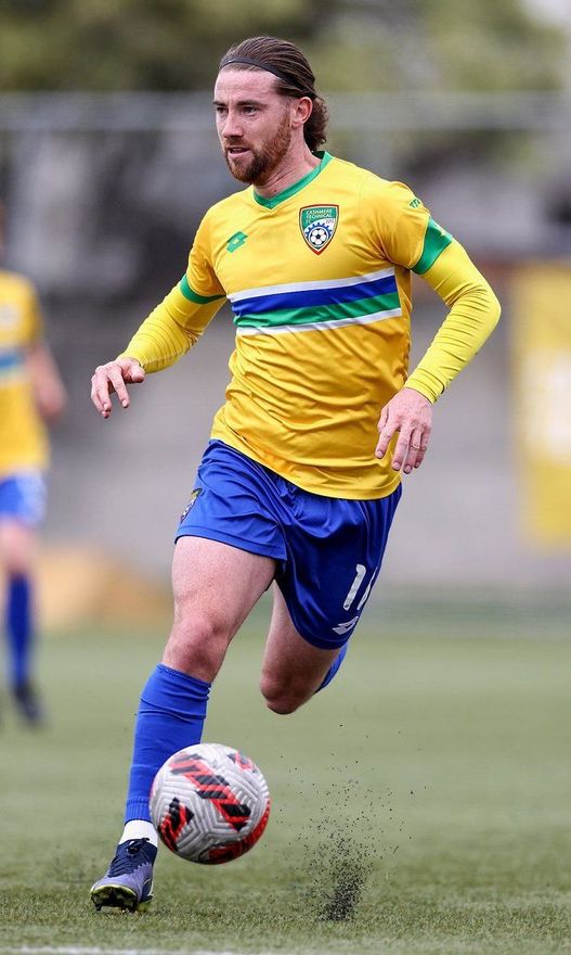 A man in a yellow shirt and blue shorts is kicking a soccer ball on a field.