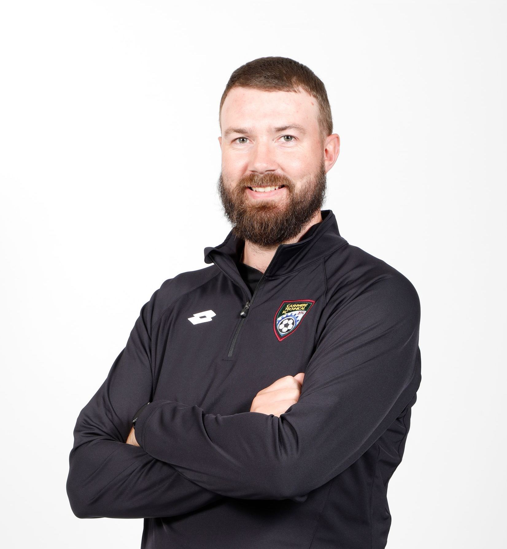 A man with a beard is wearing a blue jacket with his arms crossed.