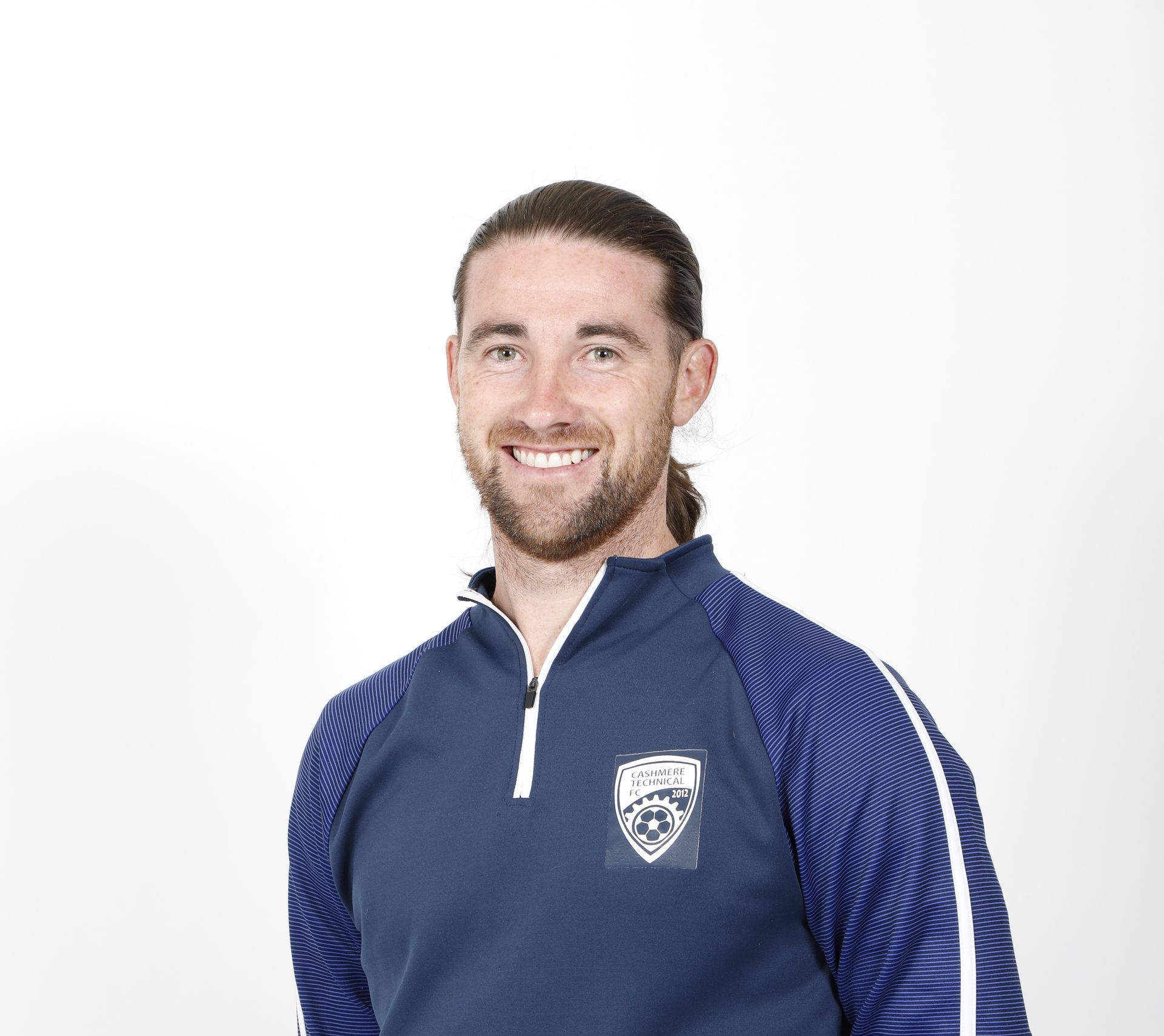 A man with a beard is wearing a blue jacket and smiling.