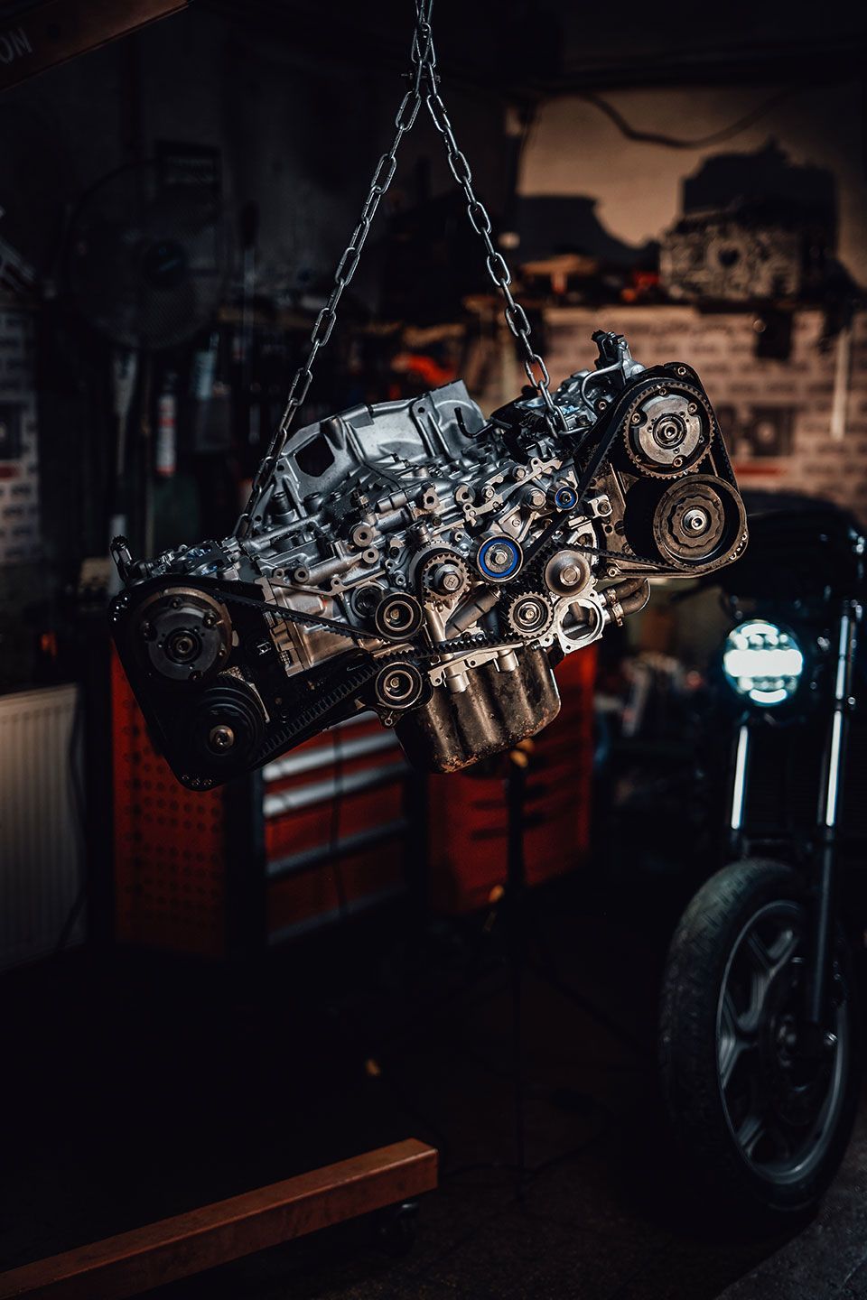A motorcycle engine is hanging from chains in a garage.